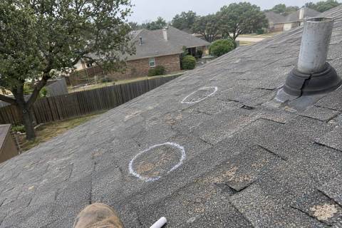 Worn gray asphalt shingles with bald patches and two chalk circles drawn on the slope, a vent pipe with a cracked collar to one side