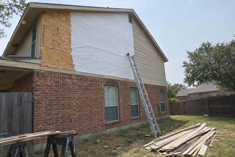 Second-story wall above brick with old siding removed from half of it, white wrap over the sheathing, new lap boards going up and a ladder against the wall