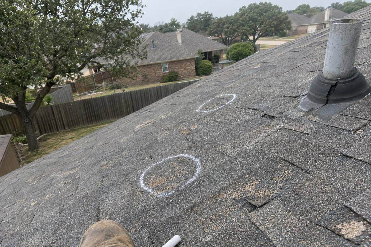 Worn gray asphalt shingles with bald patches and two chalk circles drawn on the slope, a vent pipe with a cracked collar to one side